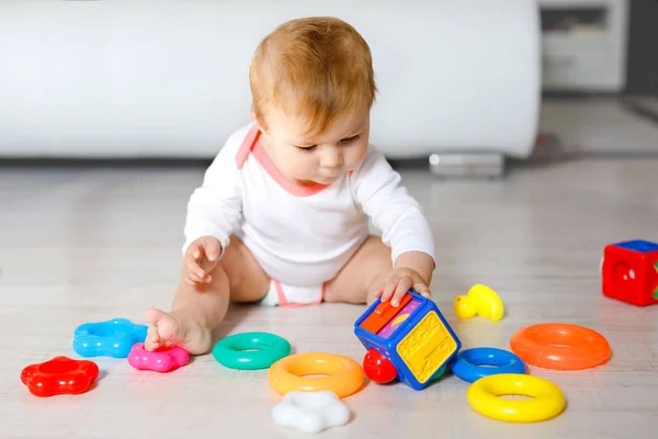 Bebek kız kreş eğitici oyuncaklar ile oynama. Mutlu sağlıklı çocuk evde renkli yumuşak oyuncaklar ile eğleniyor. Evlat plastik piramit inşa etmeye ve harflerle bloğu kullanma — Stok fotoğraf