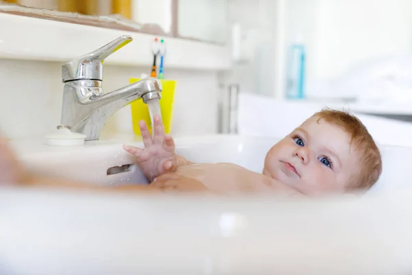 Schattige schattig baby nemen bad in wassen gootsteen en waterkraan pak. — Stockfoto