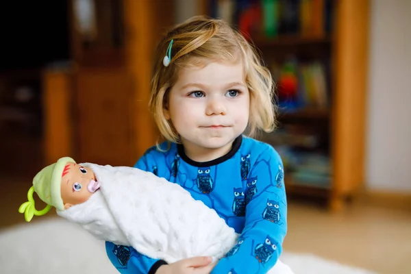 Αξιολάτρευτο χαριτωμένο κοριτσάκι που παίζει με την κούκλα. Ευτυχισμένο υγιές μωρό παιδί που διασκεδάζει με το παιχνίδι ρόλων, παίζοντας τη μητέρα στο σπίτι ή το νηπιαγωγείο. Ενεργή κόρη με παιχνίδι. — Φωτογραφία Αρχείου