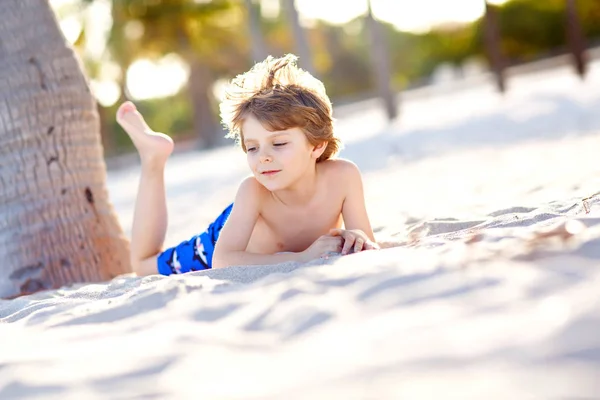 Niño rubio divirtiéndose en la playa de Miami, Key Biscayne. Feliz niño lindo saludable jugando con arena y corriendo cerca del océano. Palmeras, casa de seguridad y arena blanca. Con luz brillante cálida y soleada — Foto de Stock