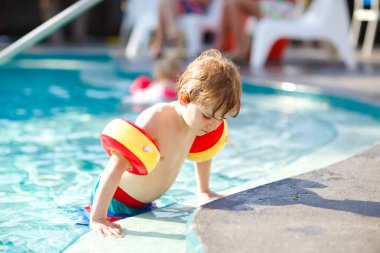 Mutlu küçük çocuk çocuk yüzme havuzuna eğleniyor. Yüzmeyi öğrenme etkin mutlu sağlıklı okul öncesi çocuk. güvenli floaties veya swimmies ile. Aile, tatil, yaz konsepti