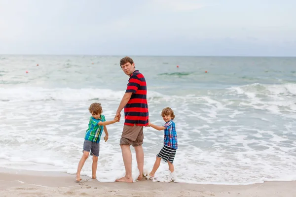 Dvě malé děti chlapci a otec na pláži oceánu — Stock fotografie