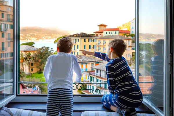 Dos niños pequeños disfrutando de la vista desde la ventana de la mañana en la región de Liguria en Italia. Impresionantes pueblos de Cinque Terre y Portofino. Vacaciones en familia en la hermosa ciudad italiana con casas coloridas . — Foto de Stock