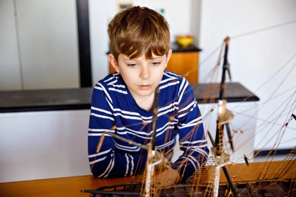 Küçük sarışın okul çocuk çocuk kapalı yelkenli gemi modeli ile oynuyor. Yatlı heyecanlı çocuk okuldan sonra evde eğleniyor. Mutlu çocuk bina ve oyuncaklar oluşturma — Stok fotoğraf