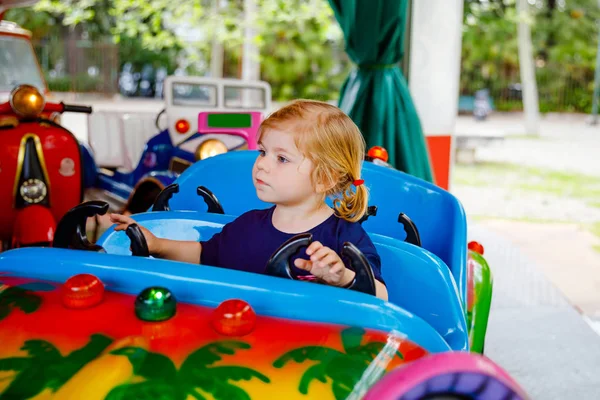 Adorabile bambina che cavalca su un'auto divertente sulla giostra rotonda nel parco divertimenti. Buon bambino sano divertirsi all'aperto nella giornata di sole. Weekend in famiglia o vacanze — Foto Stock