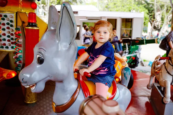 Rozkošná malá holčička na koni na kolotoče v zábavním parku. Šťastné a zdravé dítě se baví venku za slunečného dne. Rodinný víkend nebo dovolená — Stock fotografie