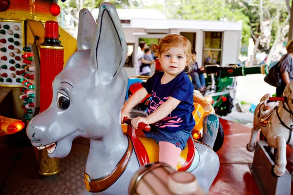 Rozkošná malá holčička na koni na kolotoče v zábavním parku. Šťastné a zdravé dítě se baví venku za slunečného dne. Rodinný víkend nebo dovolená — Stock fotografie