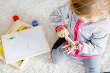 Küçük kızın keçeli kalemle resim yapmayı öğrenmesine çok az kaldı. Ellerine ve kıyafetlerine resim çizen küçük bebek..
