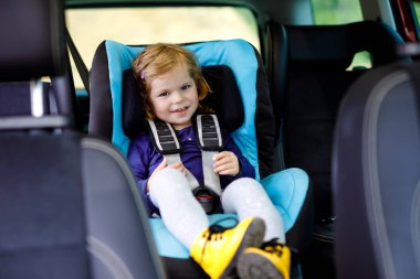 Araba güvenlik koltuğunda oturan mavi gözlü sevimli kız bebek. Küçük çocuk aile tatillerine ve jorney'e gidiyor. Renkli giysiler ve sarı ayakkabı mutlu sağlıklı çocuk.