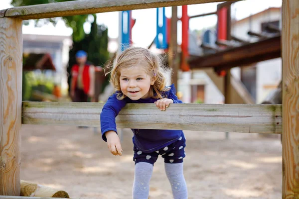 Menina da criança bonito se divertindo no parque infantil. Criança pequena saudável feliz escalada, balançando e deslizando em equipamentos diferentes. No dia ensolarado em roupas coloridas. Jogo ao ar livre ativo para crianças — Fotografia de Stock