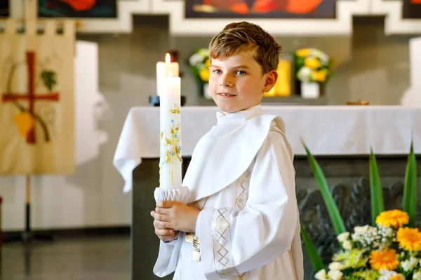 彼の最初の聖なる交わりを受けている小さな子供の男の子。キリスト教のろうそくを持つ幸せな子供。カトリックの呪いの伝統。祭壇の近くの教会で白い伝統的なガウンの子供. — ストック写真