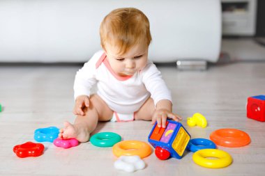 Bebek kız kreş eğitici oyuncaklar ile oynama. Mutlu sağlıklı çocuk evde renkli yumuşak oyuncaklar ile eğleniyor. Evlat plastik piramit inşa etmeye ve harflerle bloğu kullanma