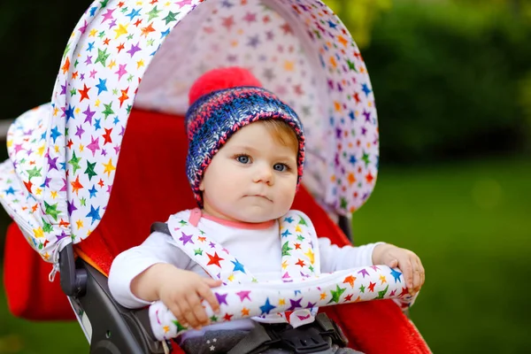Bonito saudável pequena menina bonita com chapéu quente azul sentado no carrinho de bebê ou carrinho e esperando a mãe. Criança sorridente feliz com olhos azuis. bebê filha indo para um passeio com a família — Fotografia de Stock