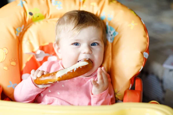 Cute little baby girl eating bread. Child eating for the first time piece of pretzel. First food after breastfeeding. Healthy baby having fun.