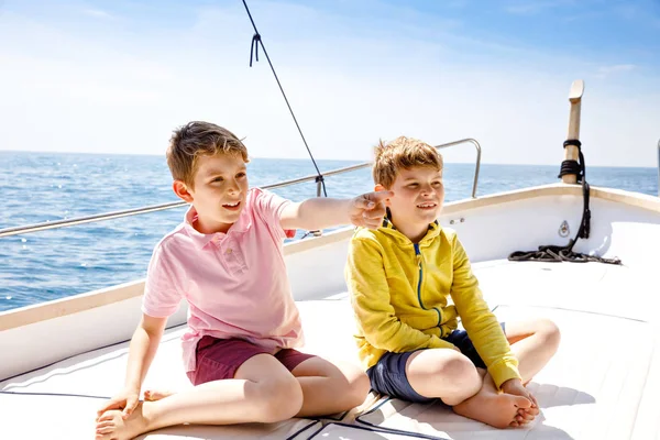 Two little kid boys, best friends enjoying sailing boat trip. Family vacations on ocean or sea on sunny day. Children smiling. Brothers, schoolchilden, siblings having fun on yacht.