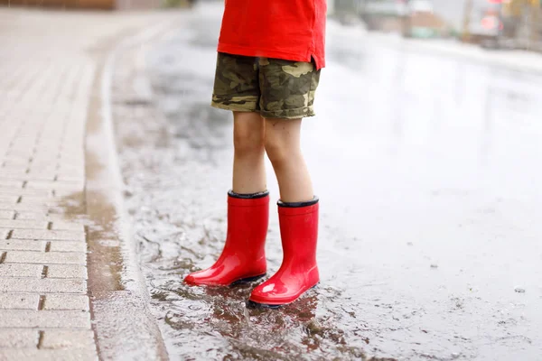Дитина в червоних дощових черевиках стрибає в калюжу . — стокове фото