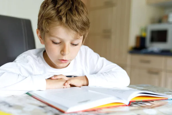 Liten blond skola unge pojke en bok hemma — Stockfoto