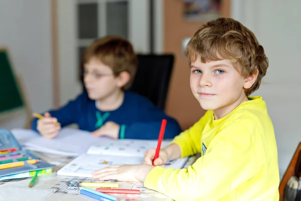 Два маленьких мальчика дома делают домашнее задание. Маленькие сосредоточенные дети пишут цветными карандашами в помещении. Начальная школа и образование. Братья и сестры и лучшие друзья учатся . — стоковое фото