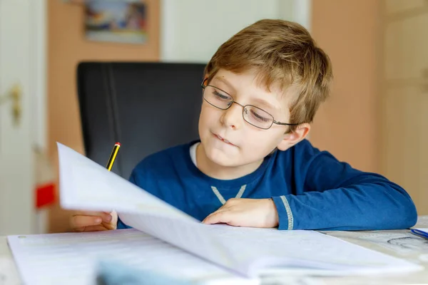 Portret van schattige school jongen jongen met bril thuis maken van huiswerk. Weinig geconcentreerd kind schrijven met kleurrijke potloden, binnenshuis. Basisschool en onderwijs — Stockfoto