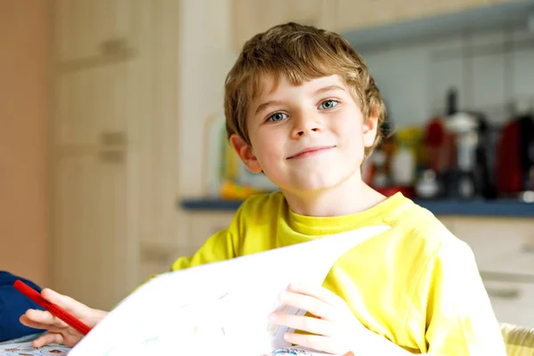 Portrait of cute school kid boy at home making homework. Little concentrated child writing with colorful pencils, indoors. Elementary school and education. Kid learning writing letters and numbers.