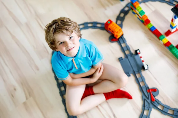 Menino garoto loiro brincando com blocos de plástico coloridos e criando estação de trem — Fotografia de Stock