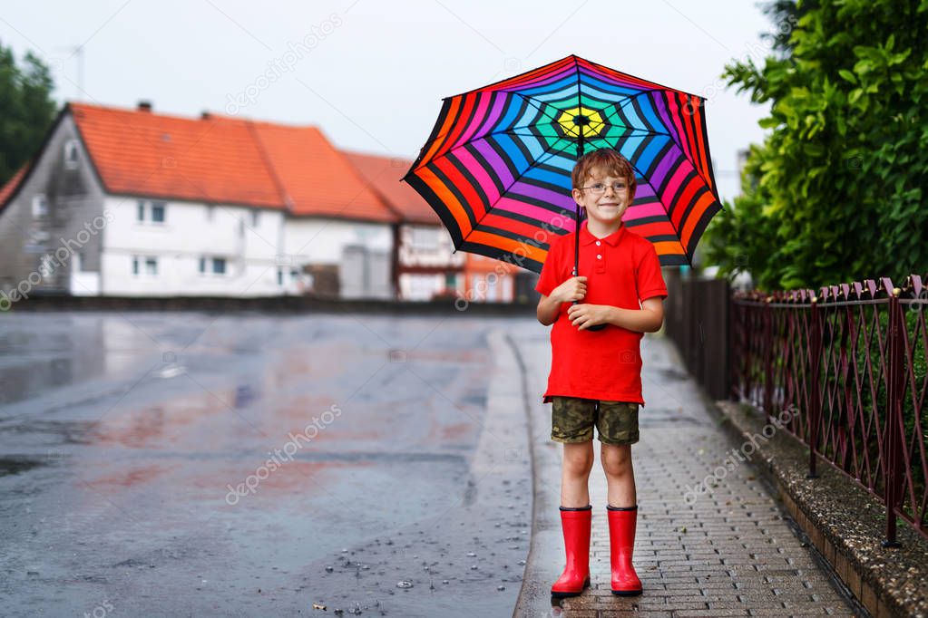 Kid boy wearing red rain boots and walking with umbrella