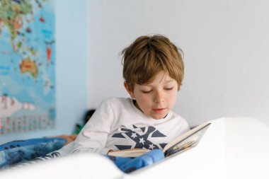 Sevimli sarışın küçük çocuk çocuk pijama onun yatak odasında kitap okuma
