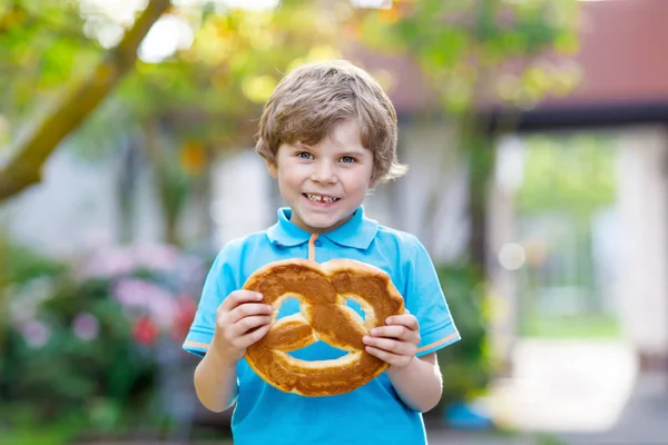 Adorable little kid boy eating huge big bavarian german pretzel. — Stock Photo, Image