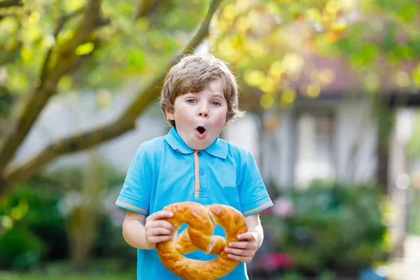 Liebenswerter kleiner Junge isst riesige große bayerische Brezel. — Stockfoto