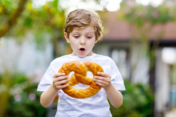 愛らしい小さな男の子食べる巨大な大規模な野蛮ドイツ語のプレッツェル. — ストック写真