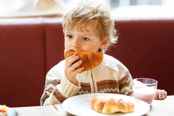 Niedlichen gesunden Jungen essen Croissant und trinken Erdbeer-Milchshake im Café. glückliches Kind beim Frühstück mit den Eltern oder im Kinderzimmer. Gemüse, Eier als gesunde Nahrung für Kinder. — Stockfoto