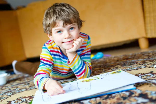 Menino pré-escolar em casa fazendo lição de casa, pintando uma história com canetas coloridas — Fotografia de Stock