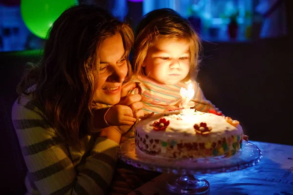 Adorable niñita celebrando su segundo cumpleaños. Bebé hija y madre joven soplando velas en la torta y velas. Feliz retrato familiar saludable, mamá amor y felicidad —  Fotos de Stock