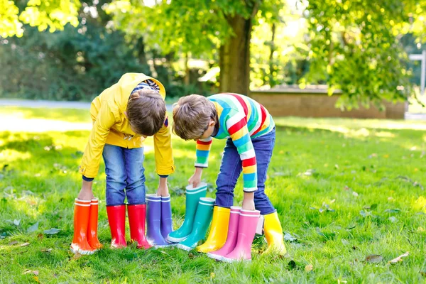 Two little kids boys, cute siblings with lots of colorful rain boots. Children in different rubber boots and jackets. Footwear for rainy fall. Healthy twins and best friends having fun outdoors — Stock Photo, Image