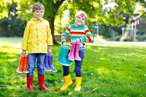 Dos niños pequeños, hermanos lindos con muchas botas de lluvia de colores. Niños en diferentes botas de goma y chaquetas. Calzado para otoño lluvioso. Gemelos sanos y mejores amigos divirtiéndose al aire libre — Foto de Stock