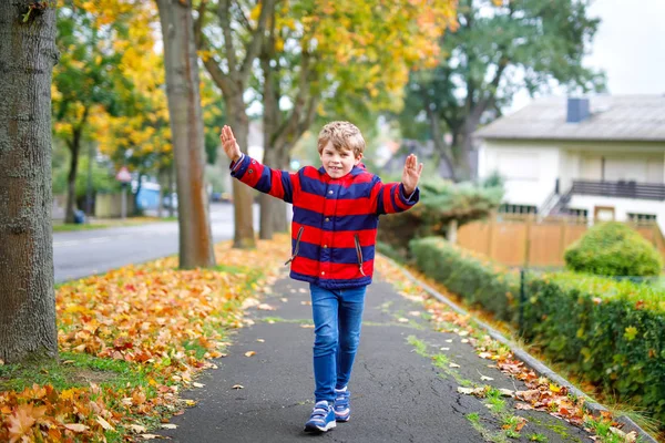 Fröhlicher kleiner Junge, der nach der Schule auf der herbstlichen Straße läuft. Kind freut sich über Schulferien. Kind mit Herbstmode spaziert durch die Stadt. — Stockfoto