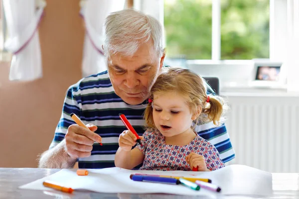 Cute little baby toddler girl and handsome senior grandfather painting with colorful pencils at home. Grandchild and man having fun together — Stock Photo, Image