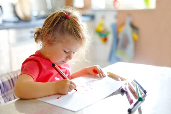 Милая маленькая девочка малышка рисует с красочными карандашами дома. Очаровательный здоровый счастливый ребенок учится рисовать, используя ручки войлочных наконечников. Активный ребенок веселится в помещении или в детской. — стоковое фото