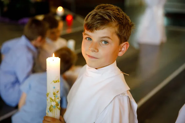 Kleiner Junge, der seine erste heilige Kommunion empfängt. glückliches Kind mit Taufkerze. Tradition in der katholischen Kirche. Kind in weißer Tracht in einer Kirche in der Nähe des Altars. — Stockfoto