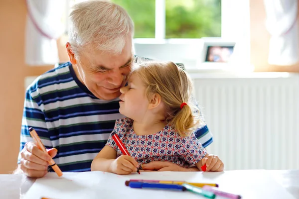 Cute little baby toddler girl and handsome senior grandfather painting with colorful pencils at home. Grandchild and man having fun together — Stock Photo, Image