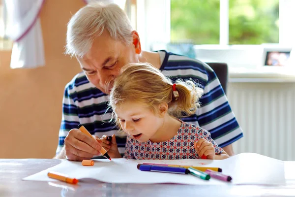 Cute little baby toddler girl and handsome senior grandfather painting with colorful pencils at home. Grandchild and man having fun together — Stock Photo, Image