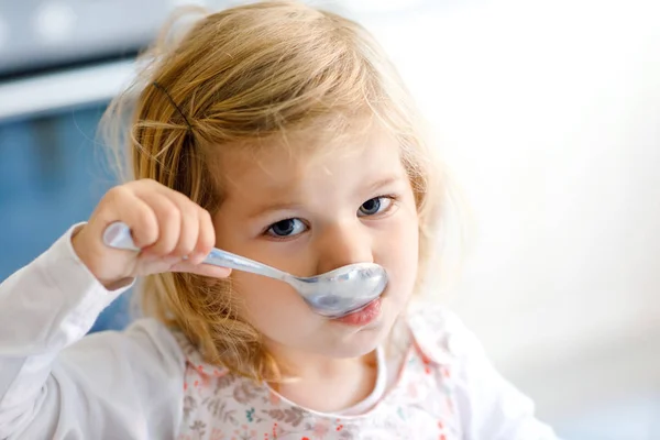 Entzückendes Kleinkind, das Suppe vom Löffel isst. niedliche glückliche Baby-Kind in bunten Kleidern in der Küche sitzen und essen. Zuhause drinnen — Stockfoto