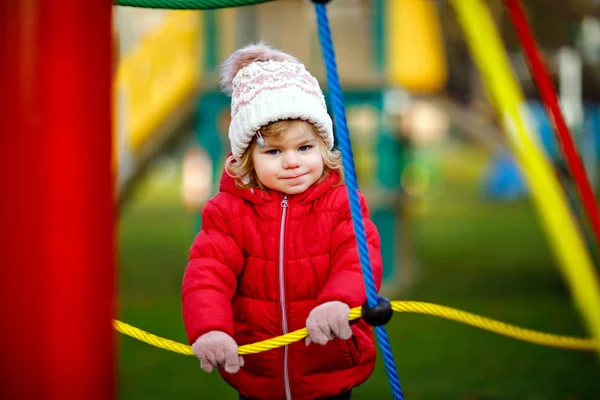 Schattig peutermeisje dat plezier heeft op de speelplaats. Gelukkige gezonde kleine kind klimmen, schommelen en glijden op verschillende apparatuur. Op koude dag in kleurrijke kleren. Actief buitenspel voor kinderen — Stockfoto