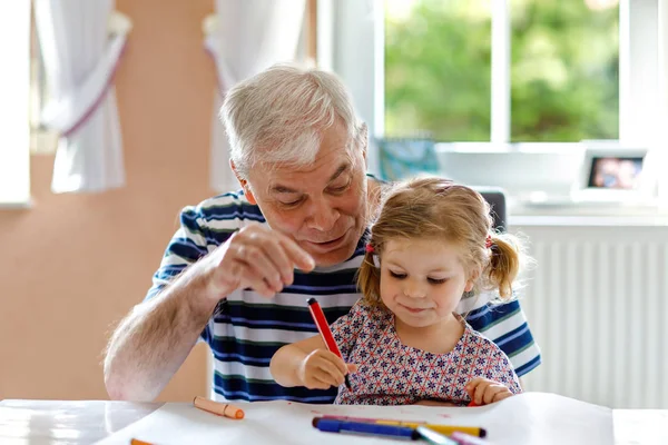 Cute little baby toddler girl and handsome senior grandfather painting with colorful pencils at home. Grandchild and man having fun together — Stock Photo, Image