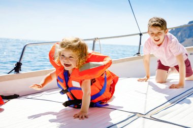 İki küçük çocuk erkek ve küçük kız yelkenli tekne gezisi zevk. Güneşli bir günde okyanus ta denizde aile tatilleri. Çocuklar gülümsüyor. Kardeşler, yatta eğlenen kardeşler.