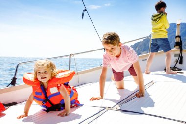 İki küçük çocuk erkek ve küçük kız yelkenli tekne gezisi zevk. Güneşli bir günde okyanus ta denizde aile tatilleri. Çocuklar gülümsüyor. Kardeşler, yatta eğlenen kardeşler.