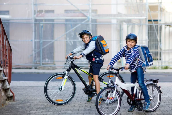 Två skolpojkar i skyddshjälm rider med cykel i staden med ryggsäckar. Glada barn i färgglada kläder cykling på cyklar på väg till skolan. Säkert sätt för barn utomhus till skolan — Stockfoto