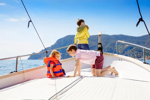 Due bambini piccoli ragazzi e la bambina godendo gita in barca a vela. Vacanze in famiglia sull'oceano o sul mare nelle giornate di sole. Bambini sorridenti. Fratelli e sorelle, fratelli e sorelle che si divertono sullo yacht . — Foto Stock