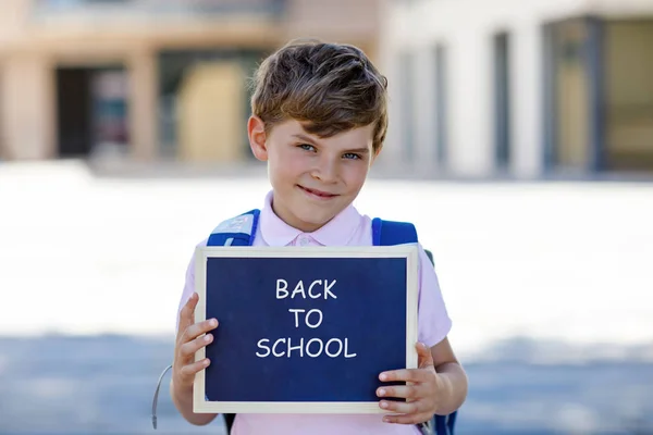 Lycklig liten unge pojke med ryggsäck eller skolväska och glasögon. Skolunge på väg till skolan. Friska bedårande barn utomhus på krita Desk bye bye skola. Tillbaka till skolans koncept — Stockfoto