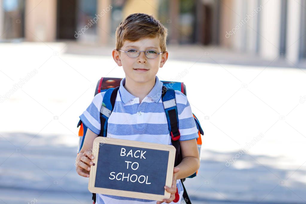 Happy little kid boy with backpack or satchel and glasses. Schoolkid on the way to school. Healthy adorable child outdoors On chalk desk Bye bye school. Back to school concept